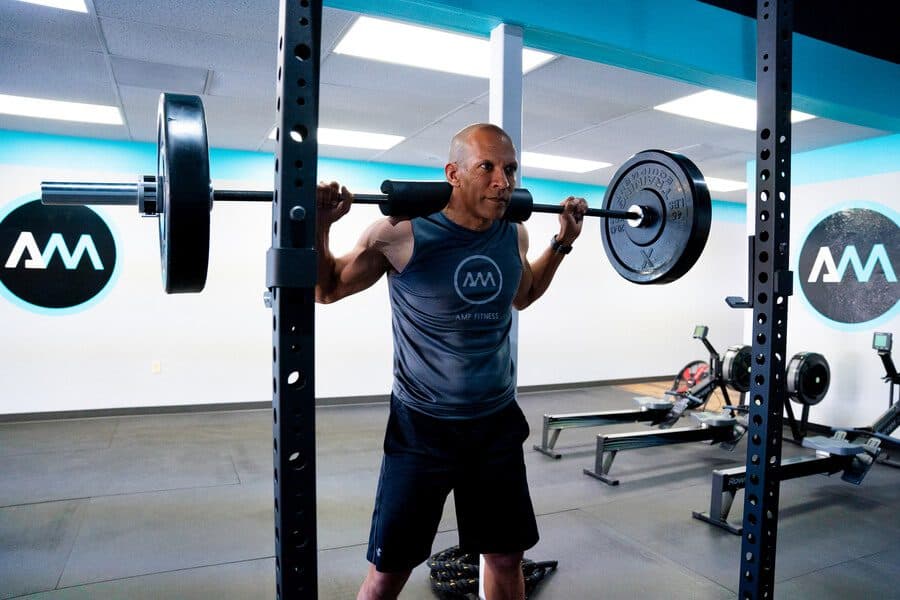 AMP Fitness member performing a barbell back squat in the Mesa, AZ studio, representing structured strength workout programs.