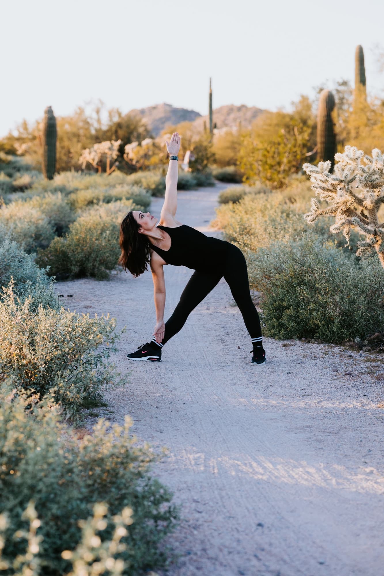 AMP Fitness yoga instructor holding a triangle pose on a desert trail near Mesa, AZ at golden hour.